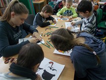 Dzieci siedzą przy stole i kolorują postacie detektywów