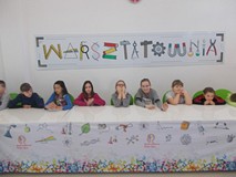 Dzieci siedzą przy stole na tle napisu Warsztatownia