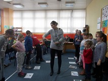 Dzieci stoją przy ilustracjach detektywów, a bibliotekarka losuje imię postaci