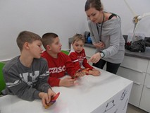 Trzech chłopców pokazuje siedzi przy stole, nad nimi stoi bibliotekarka