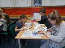 Dzieci siedzą przy stołach i wspólnie pracują nad plakatem