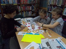 Dzieci siedzą przy stoliku i przyklejają elementy swojej pracy plastycznej do kartki