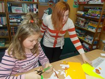 Dziewczynka wycina owoc, a bibliotekarka wspomaga jej prace
