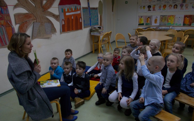 Grupa przedszkolaków słucha o przygodach Misia Uszatka. Pani bibliotekarka czyta.