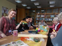 Panie siedzą przy stole z bibliotekarką, która trzyma ozdobiony koszyczek w ręku