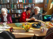 Trzy panie siedzą przy stole i pokazują swoje rękodzieła