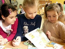 Trzy dziewczynki wspólnie oglądają książkę MAM PRZYJACIELA... PSZCZELARZA