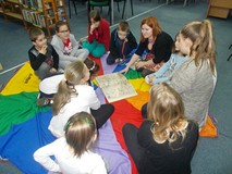 Dzieci siedzą na chuście z bibliotekarką i wspólnie oglądają książkę