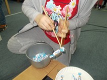 Dziecko trzyma w ręku pałeczki bambusowe i próbuje chwycić nimi cukierka