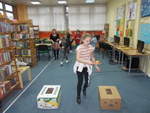 Dziewczynka biegnie z paletką i piłeczką w zawodach drużynowych, w tle stoją pozostałe dzieci