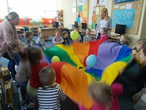 Dzieci bawią się chustą animacyjną podrzucając balony