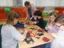 Bibliotekarka pomaga dzieciom siedzącym przy stole w wykonywaniu pracy plastycznej