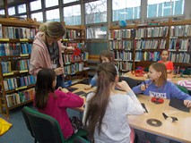 Bibliotekarka tzyma w ręku biedronkę z papieru, a dzieci siedzące przy stole ją wykonują