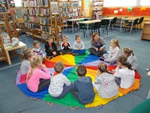 Dzieci z bibliotekarką siedzą na chuście i rozmawiają