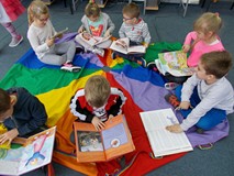 Przedszkolaki siedzą na chuście i oglądaja książeczki