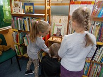 Troje dzieci szuka książek na regałach