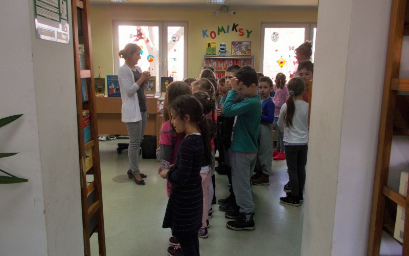 Grupa przedszkolaków stoi w sali i rozmawia z pania bibliotekarką.