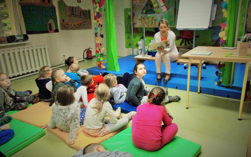 Przedszkolaki siedzą na materacach, pani bibliotekarka czyta książeczkę o przygodach...