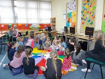 Dzieci siedzą na chuście wraz z bibliotekarką, która trzyma w ręku ilustrację