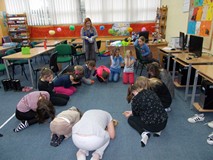 Dzieci w kręgu są skulone, a bibliotekarka losuje kartkę z pudełka