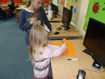 Dziewczynka odrysowuje swoją rękę na kartce papieru a dziewczynka z tyłu jej pomaga