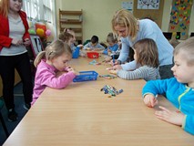 Dzieci kolorują prace przy stołach z pomocą nauczycielki