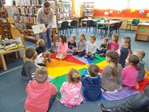 Bibliotekarka stoi nad grupą dzieci i pokazuje im książkę