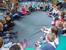 dzieci siedzą w kole i słuchają ksiązki czytanej przez bibliotekarkę