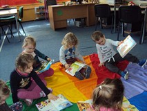 Dzieci siedzą na chuście animacyjnej i oglądają książki