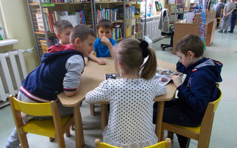 Kilkoro dzieci przy stoliku ogląda ksiązki