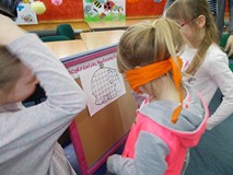 Dziewczynka z zawiązanymi oczami dorysowuje słoniowi trąbę. Pozostałe dzieci stoją przy niej