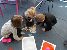 Troje dzieci układa obrazek z rozsypanych elementów