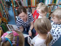 Dzieci stoją wokół bibliotekarki czytającej książkę