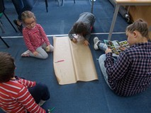 Dzieci pracują w grupie i zapisują odpowiedzi na szarym papierze