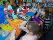 Dzieci siedzą przy stole i wycinają gotowe elementy prac