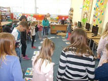 Dzieci stoją przed biblioekarką, która tłumaczy im zabawę