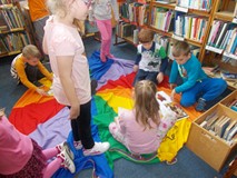 Dzieci oglądają książki siedząc na kolorowej chuście animacyjnej