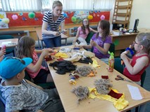 Bibliotekarka pomaga dzieciom siedzącym przy stoliku  w wykonywaniu pracy plastycznej