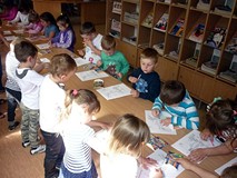 Dzieci stoją przy stolikach i kolorują wizerunek królika