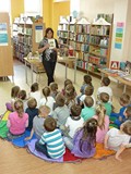 Dzieci siedzą na chuście animacyjnej. Bibliotekarka pokazuje książkę, której bohaterem jest AKSAMITN