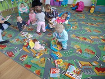 Dzieci siedzą na dywanie i w bujaczku i oglądają z nauczycielkami książki