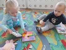 Dwoje dzieci siedzi na dywanie i ogląda książeczki