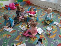 Dzieci siedzą na dywanie z nauczycielką i oglądają książki i bawią się pacynkami