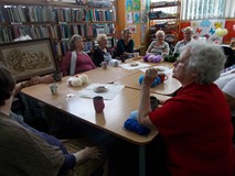 Panie z bibliotekarką siedzą przy stole i dyskutują między sobą