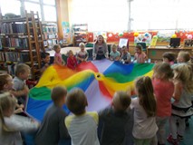 Bibliotekarka wraz z dziećmi podczas zabawy trzyma w ręku chustę animacyjną