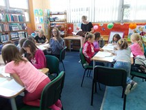 Dzieci przy stolikach rysują obrazy, a bibliotekarka czyta na głos baśń