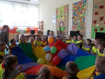 Dzieci wraz z bibliotekarką trzymają chustę i podrzucają do góry balony