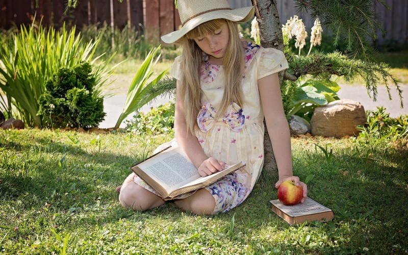Dziewczynka siedzi na trawie czytając książkę