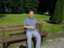 Dyrektor Koszalińskiej Biblioteki Publicznej Andrzej Ziemiński siedzi na ławce w parku i prezentuje 