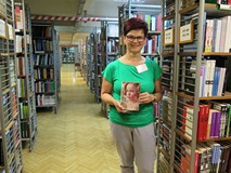 Kierowniczka Oddziału Magazynów Dorota Łobacz stoi magazynie między regałami z książkami z polecaną 